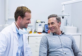 Man in chair smiling at his dentist while discussing dentures