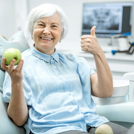 woman holding a green apple and giving a thumbs-up 