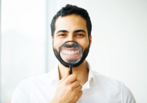 man holding magnifying glass to the veneers in his smile 